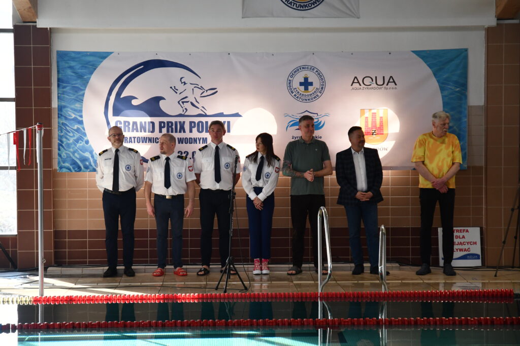 Grupa osób przy basenie, baner "Grand Prix Polski w Ratownictwie Wodnym".